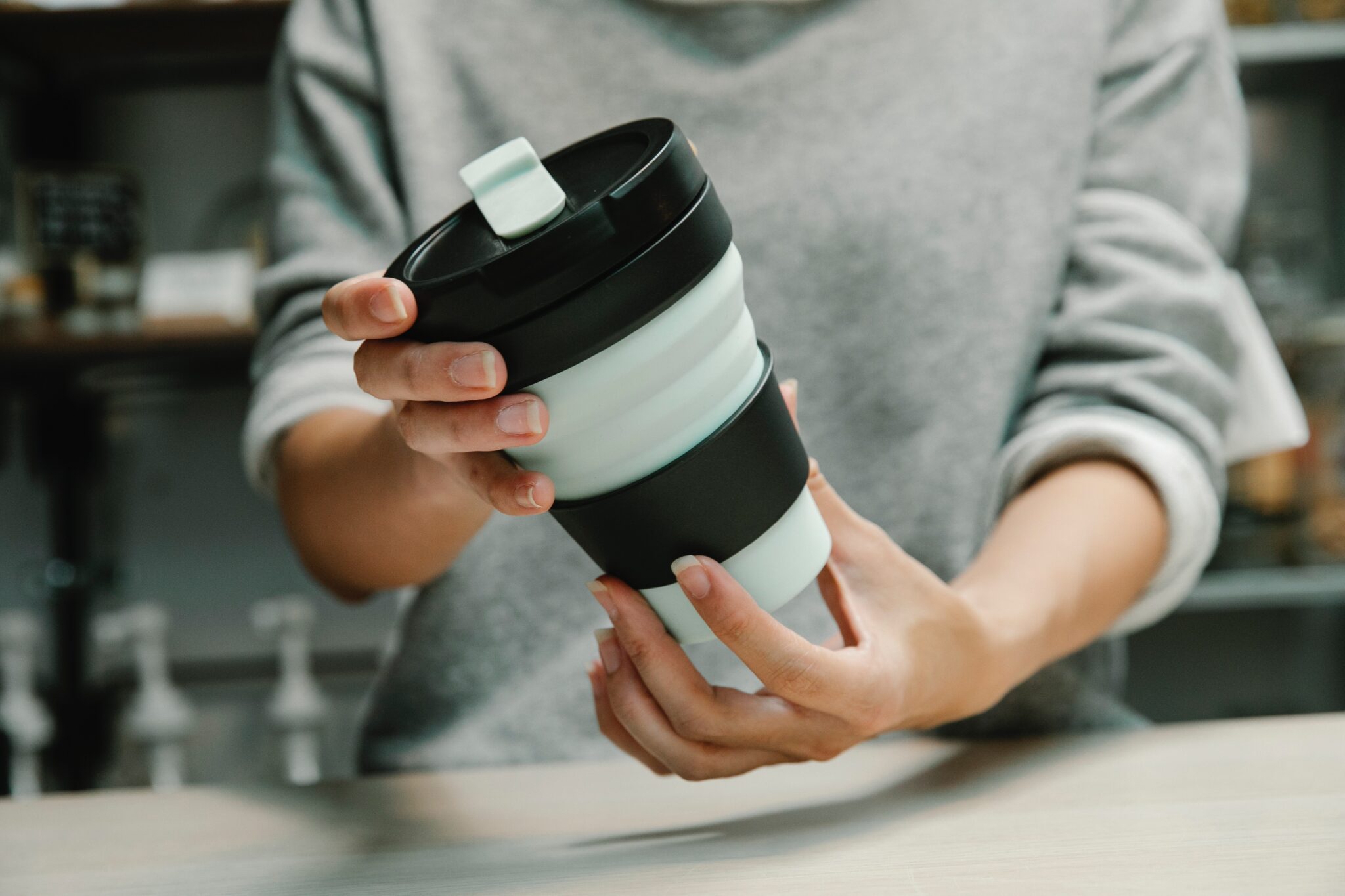カフェで reusable cup（マイタンブラー）を持参する女性の手元写真。使い捨てカップ削減やSDGs実践につながるサステナブルなライフスタイルを表現